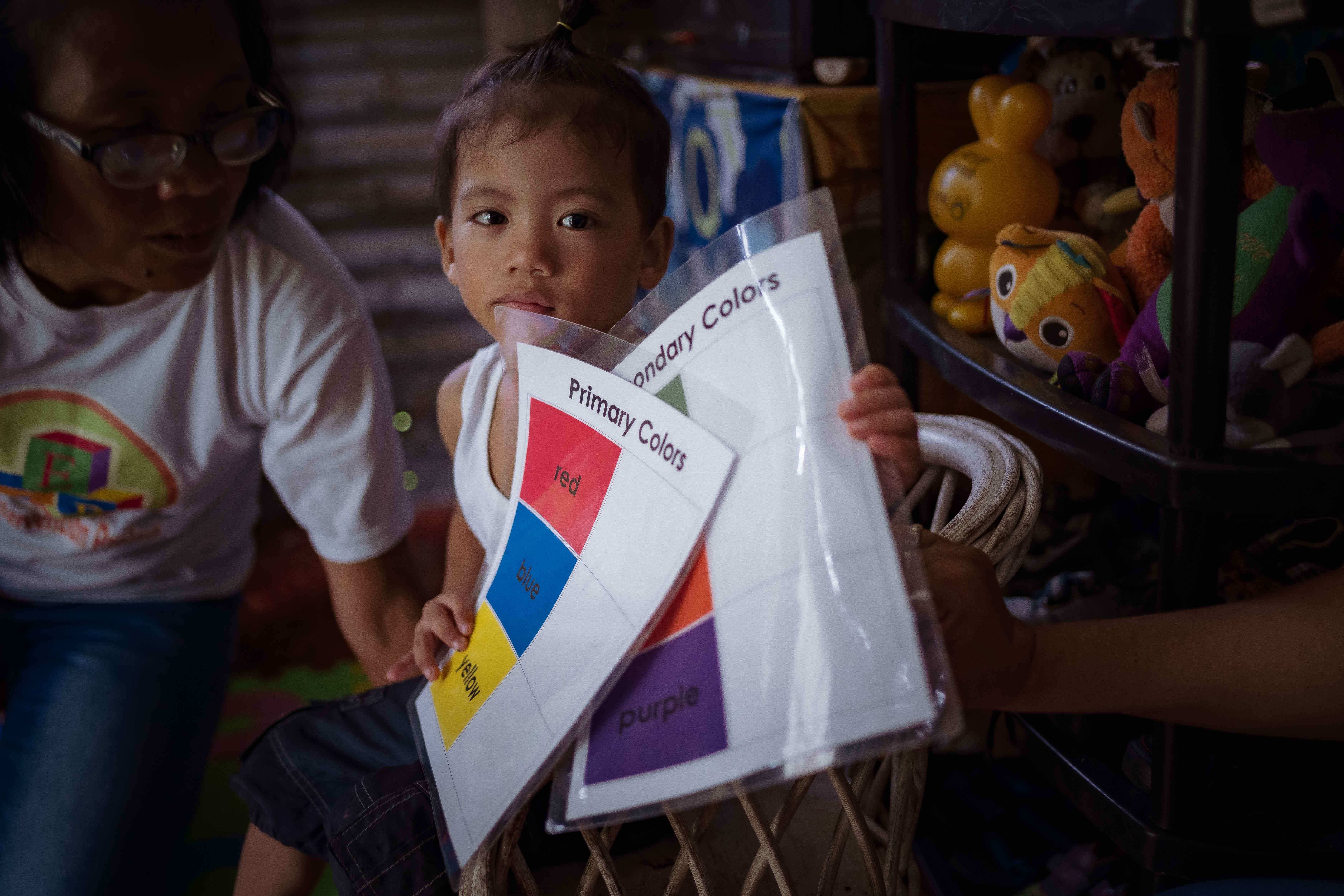 Ein kleiner Junge mit Behinderung sitzt neben seiner Trainerin und hält Lernmaterial in der Hand (Quelle: Jakob Studnar)