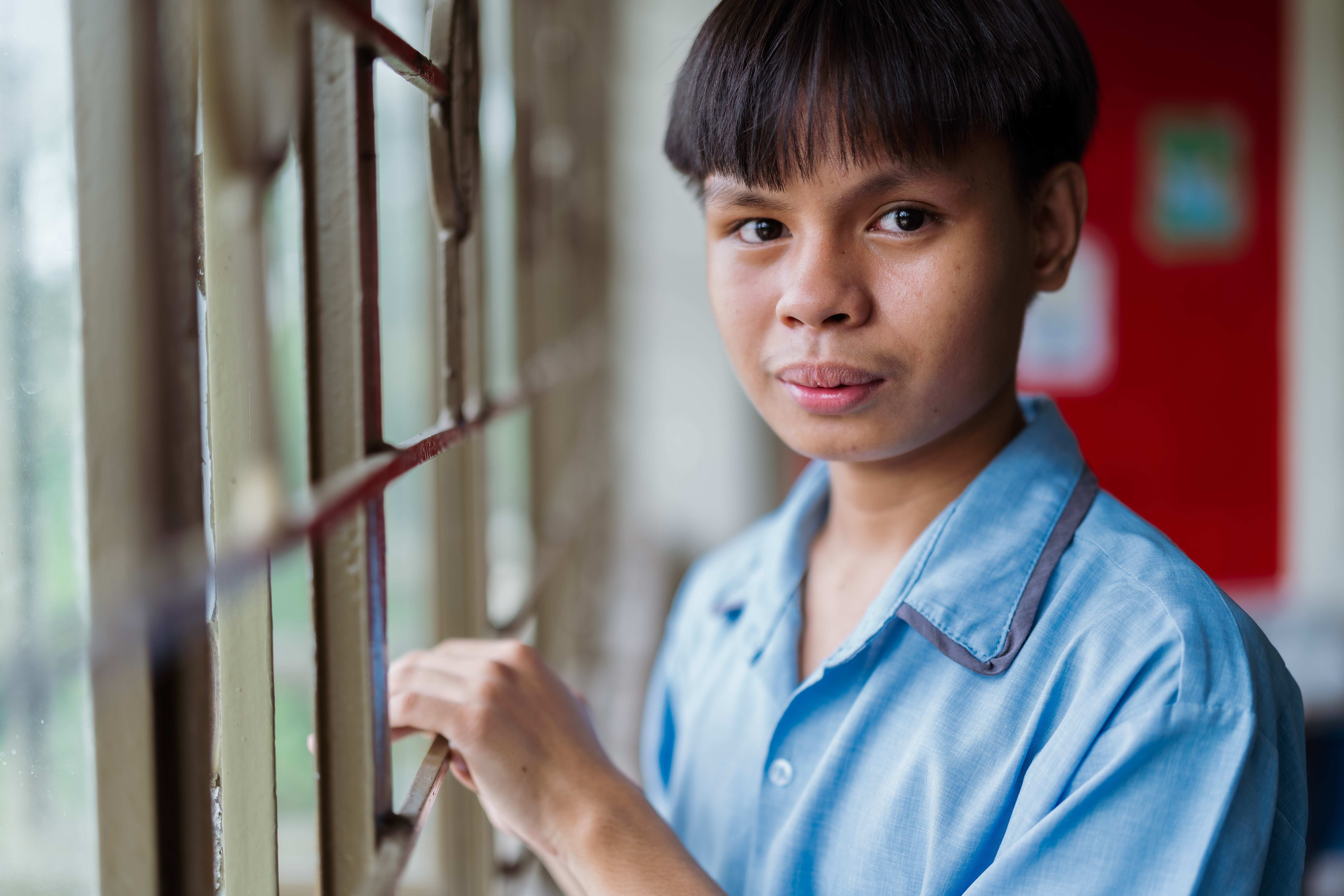 Ein Junge steht am Fenster seiner Schule und schaut ernst in die Kamera (Quelle: Jakob Studnar)