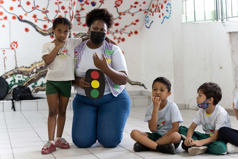 Projektleiterin Viviane Silva kniet mit einer aufgemalten Ampel in der Hand zwischen den Kindern (Quelle: Christian Nusch) Projektleiterin Viviane Silva kniet mit einer aufgemalten Ampel in der Hand zwischen den Kindern (Quelle: Christian Nusch)