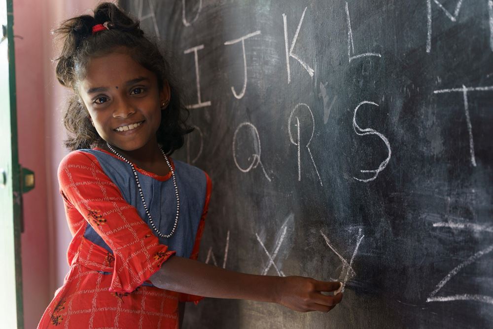 Ein Mädchen steht lachend an einer Tafel (Quelle: Christian Nusch) In den Selbsthilfegruppen lernen die Frauen auch viel über Kinderrechte (Foto: Christian Nusch)